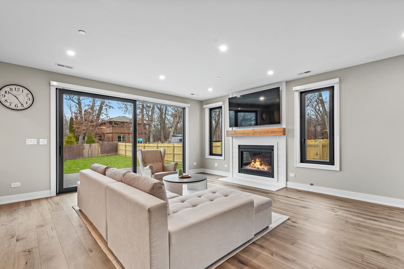 A living room with the fireplace lit, wide glass doors to the yard